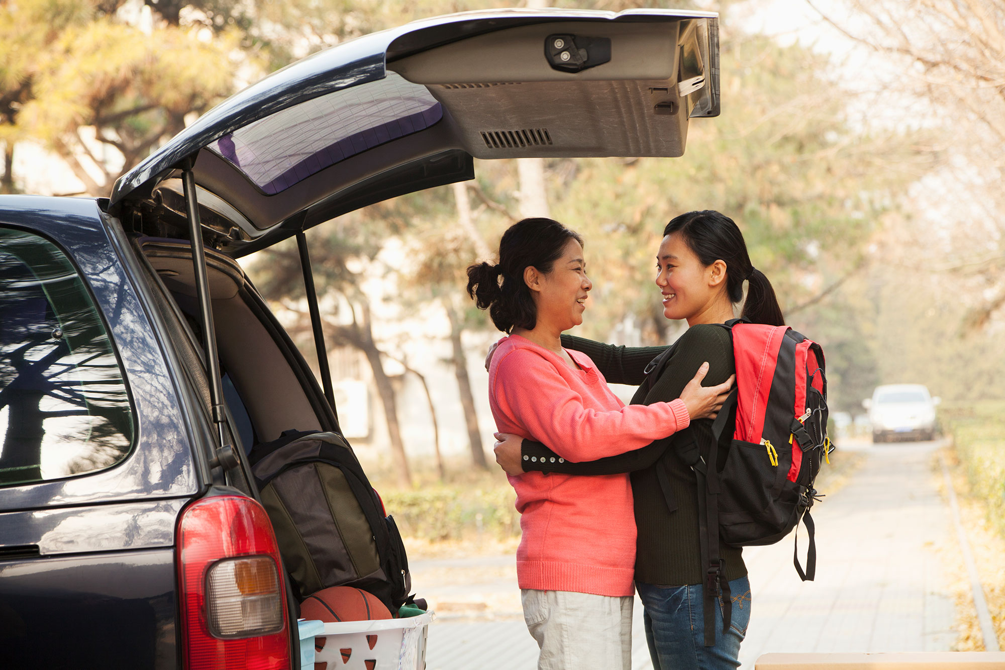Mother and daughter embracing with back hatch of car open, unpacking for college.
